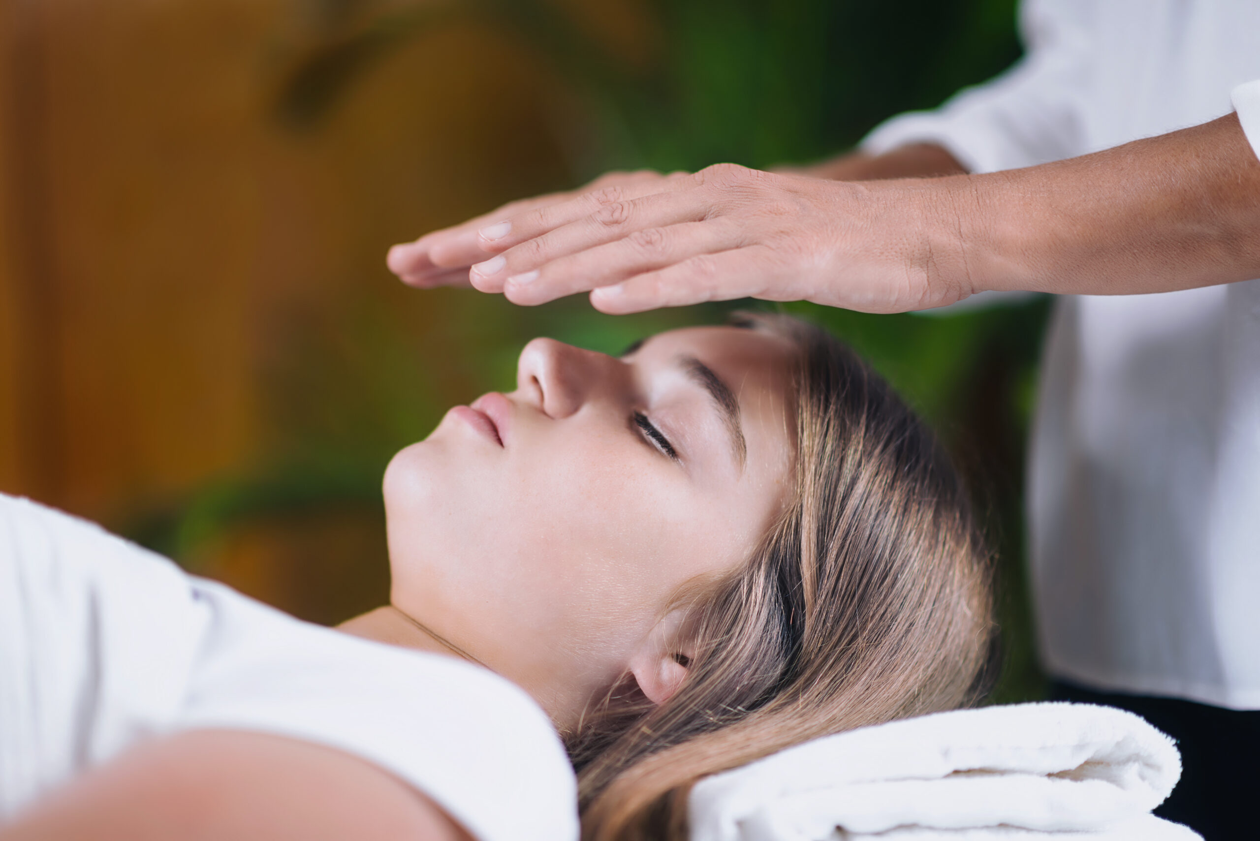 Horizontal image of Reiki therapist holding hands above head of the patient and transfer energy. Peaceful teenage girl lying with her eyes closed.